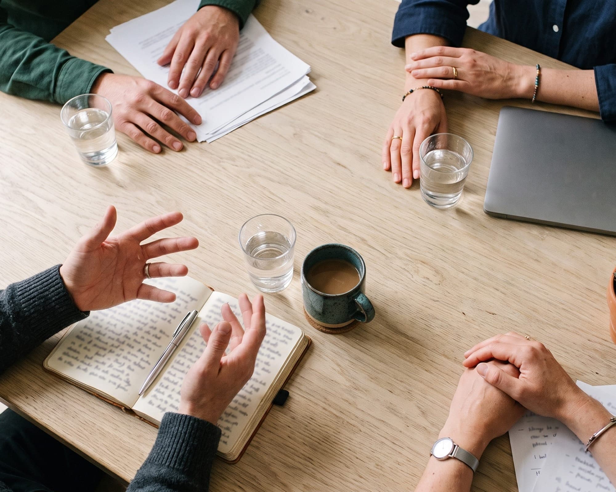 Hands of four people around a table in a working meeting, seen from above.