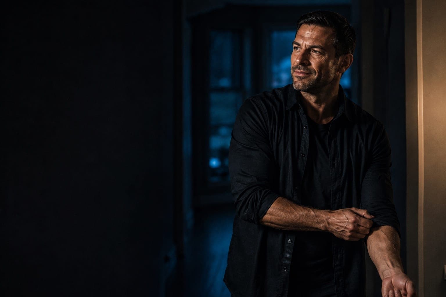 A man in his forties rolling up a sleeve in the hallway of his home in the evening.